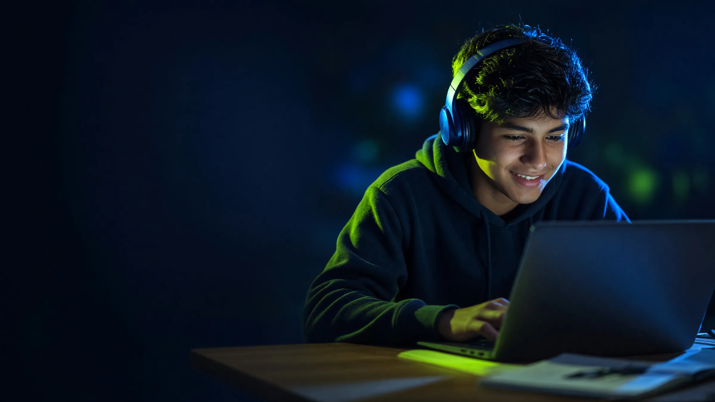 Un alumno con audífonos sonríe mientras estudia en su laptop por la noche